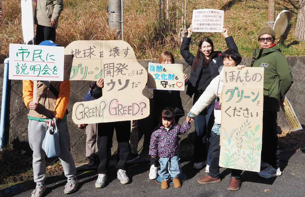 「GREEN？GREED？（緑？富に対する欲求？）」と書いたメッセージを持ってサイレントアピールする市民